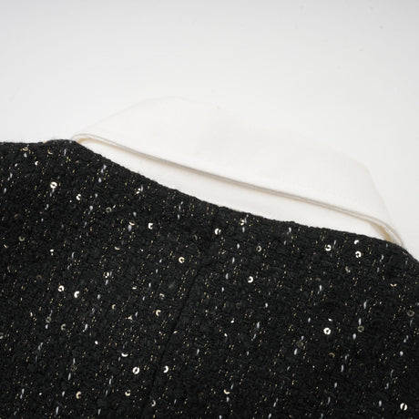 A black mini dress with a tweed fabric base featuring sequin panels on the bodice creating a sparkling contrast the dress has short sleeves and a fitted silhouette inspired by classic Audrey Hepburn style