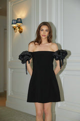A black mini dress with an offshoulder neckline featuring floral details worn by a model against a plain background