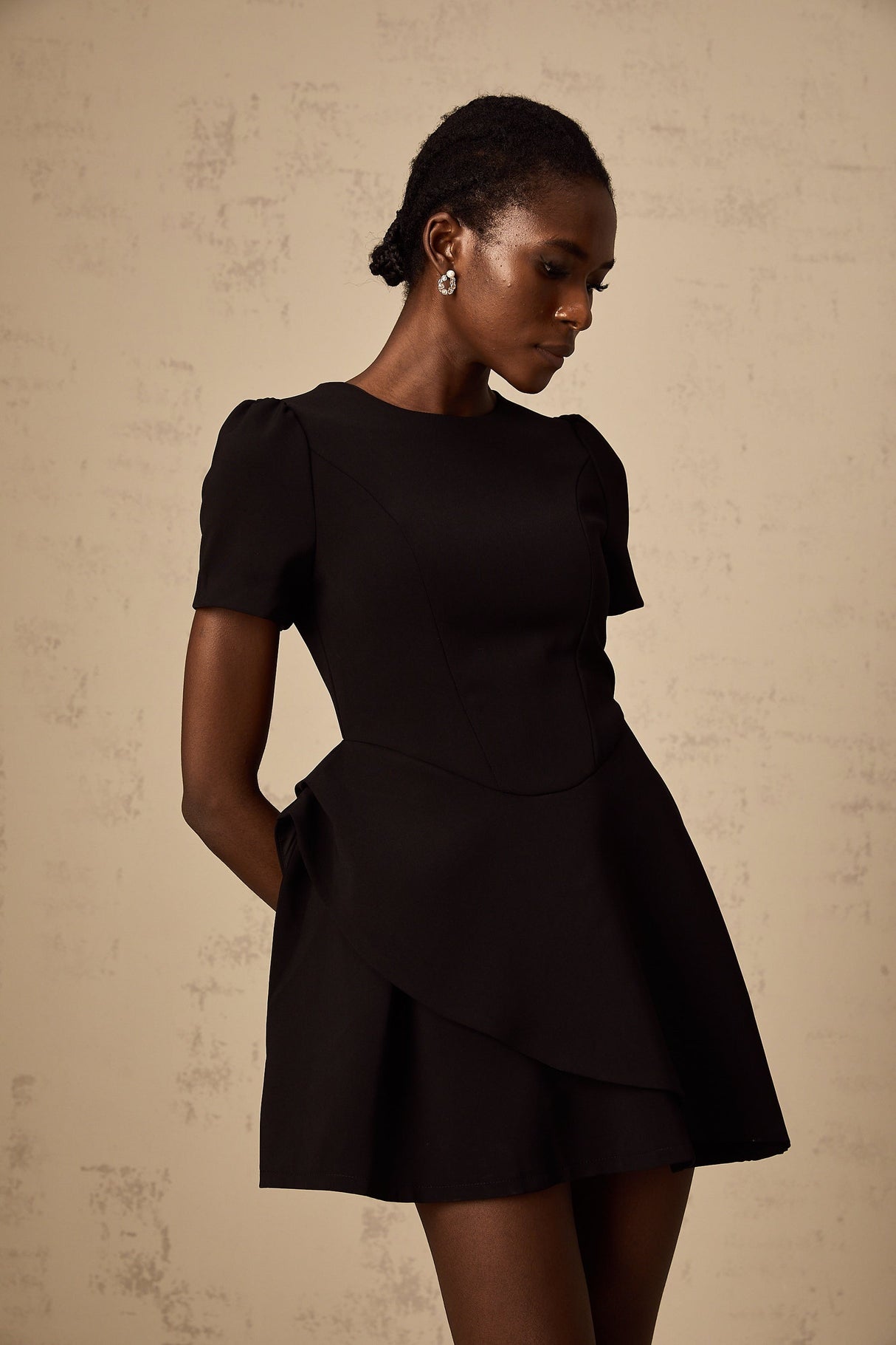 A black mini dress with asymmetric design and ruffled details named Emma