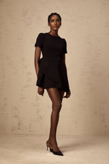 A black mini dress with asymmetric design and ruffled details worn by a model named Emma
