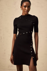 A black mini dress with decorative buttons and a fine knit texture worn by a model against a plain background