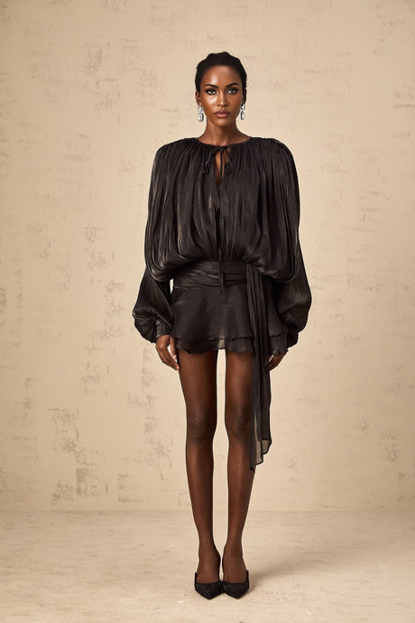 A black mini dress with full pleats and ruffled details called the Eugenie dress