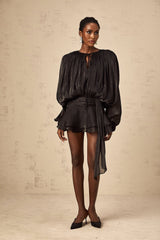A black mini dress with full pleats and ruffled details named Eugenie shown on a model or mannequin