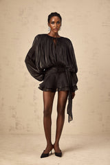 A black mini dress with full pleats and ruffled details named Eugenie shown on a plain background