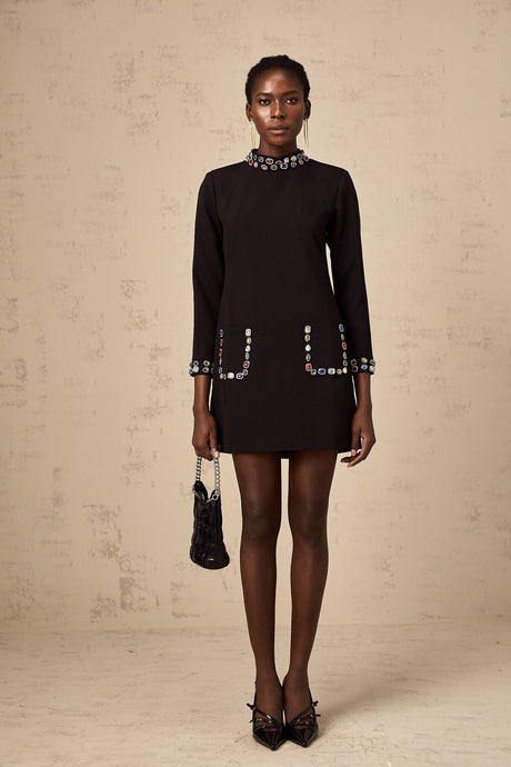 A black mini dress with long sleeves featuring crystal embellishments worn by a model against a plain background