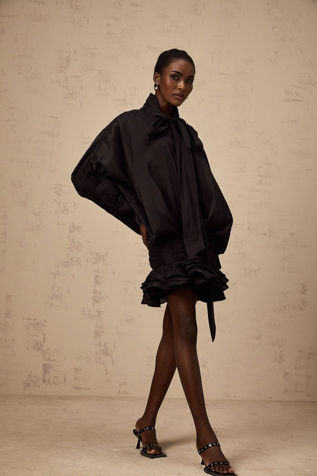 A black mini dress with ruffled details and a pussy bow neckline worn by a model