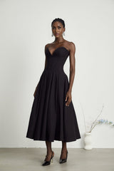 A black offshoulder midi dress with a corsetstyle bodice worn by a model standing against a plain background