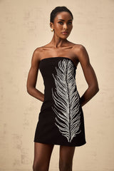 A black offshoulder mini dress with feather embellishments worn by a model against a plain background