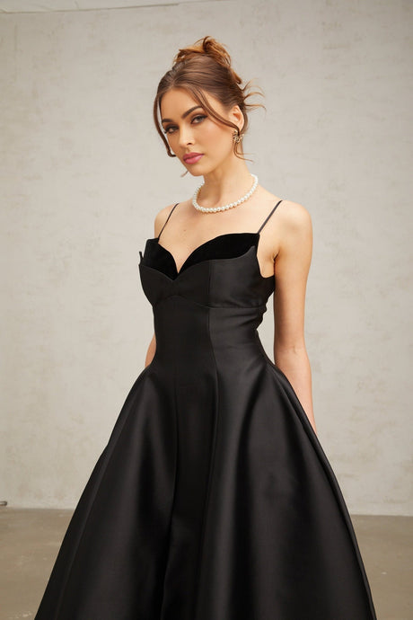 A black pleated midi dress with a flared skirt and a fitted bodice on a female model against a plain background