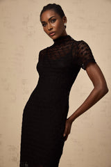 A black semi sheer knit midi dress on a mannequin or model showing the flowy silhouette and texture of the fabric