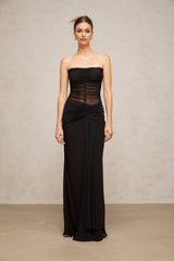 A black semi sheer maxi dress with pleated tulle fabric named Justine worn by a model standing in a neutral setting