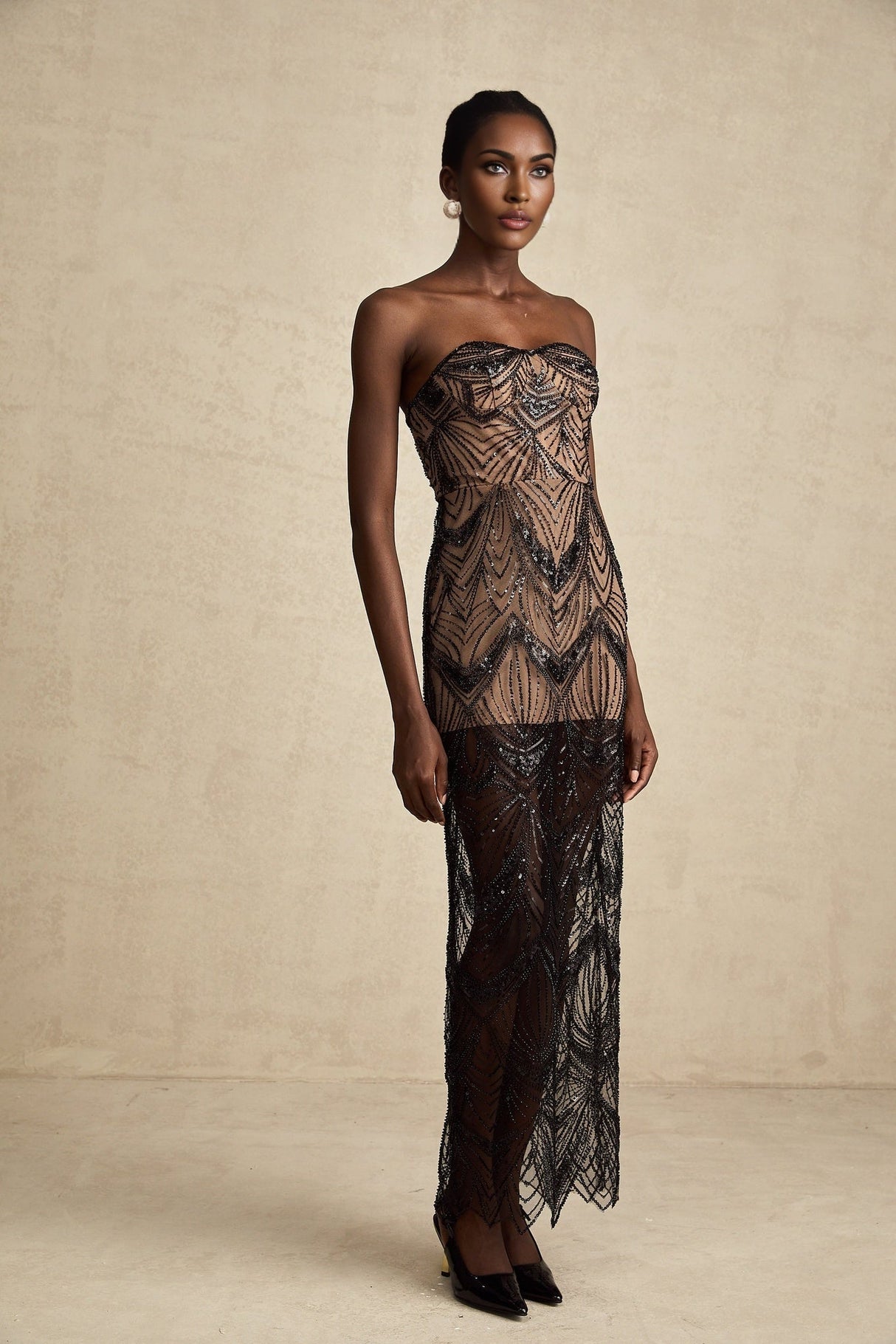 A black sequinned corset maxi dress with mesh details worn by a model standing against a plain background