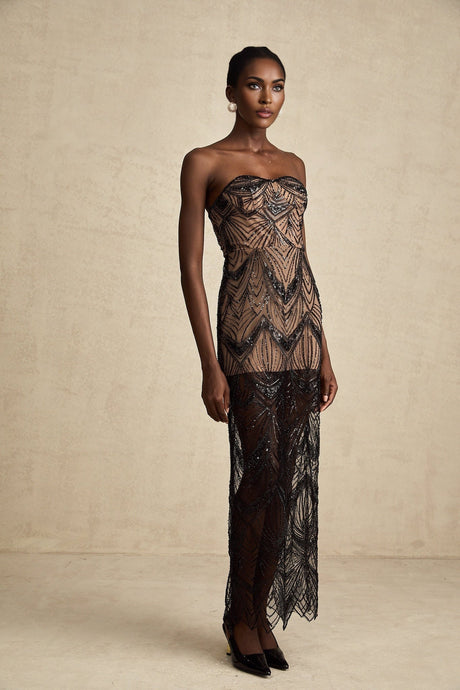 A black sequinned corset maxi dress with mesh details worn by a model standing against a plain background
