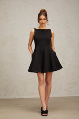 A black sleeveless mini dress with a flared skirt worn by a model standing against a plain background
