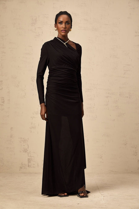 A black tulle maxi dress with an asymmetric cut and cutout details modeled by a woman standing against a plain background
