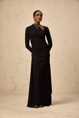 A black tulle maxi dress with asymmetric cutout details and an uneven hemline worn by a model against a plain background