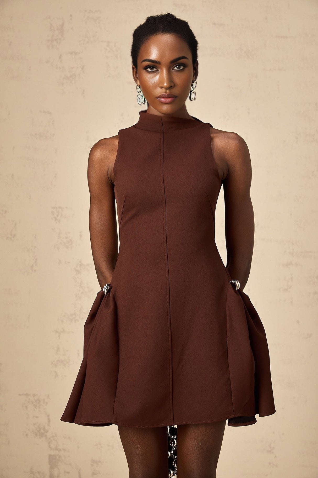 A brown mini dress with an asymmetric neckline and puff sleeves worn by a model named Dora