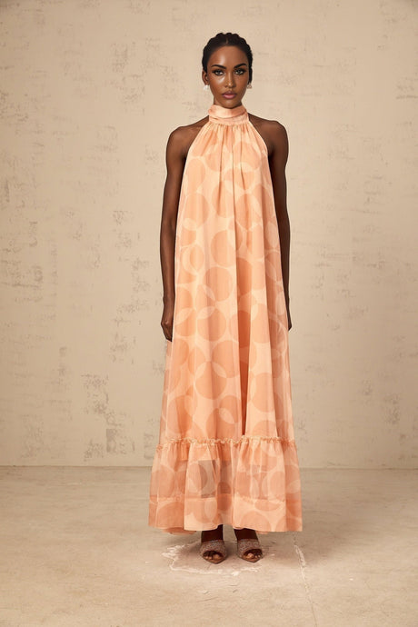 A coralpink halterneck maxi dress with a pattern print featuring a long flowing skirt and a tie around the neck named Clemence