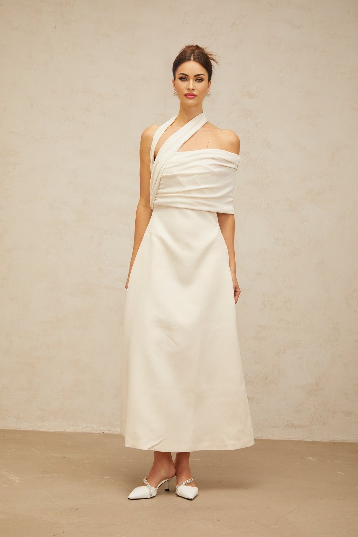 A creamwhite asymmetric maxi dress with one shoulder strap and a flowing skirt featuring a side slit