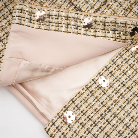 A gold tweed jacket and skirt set with sequin embellishments The jacket has long sleeves and the skirt is short Both pieces feature a textured tweed fabric with shimmering gold sequins throughout