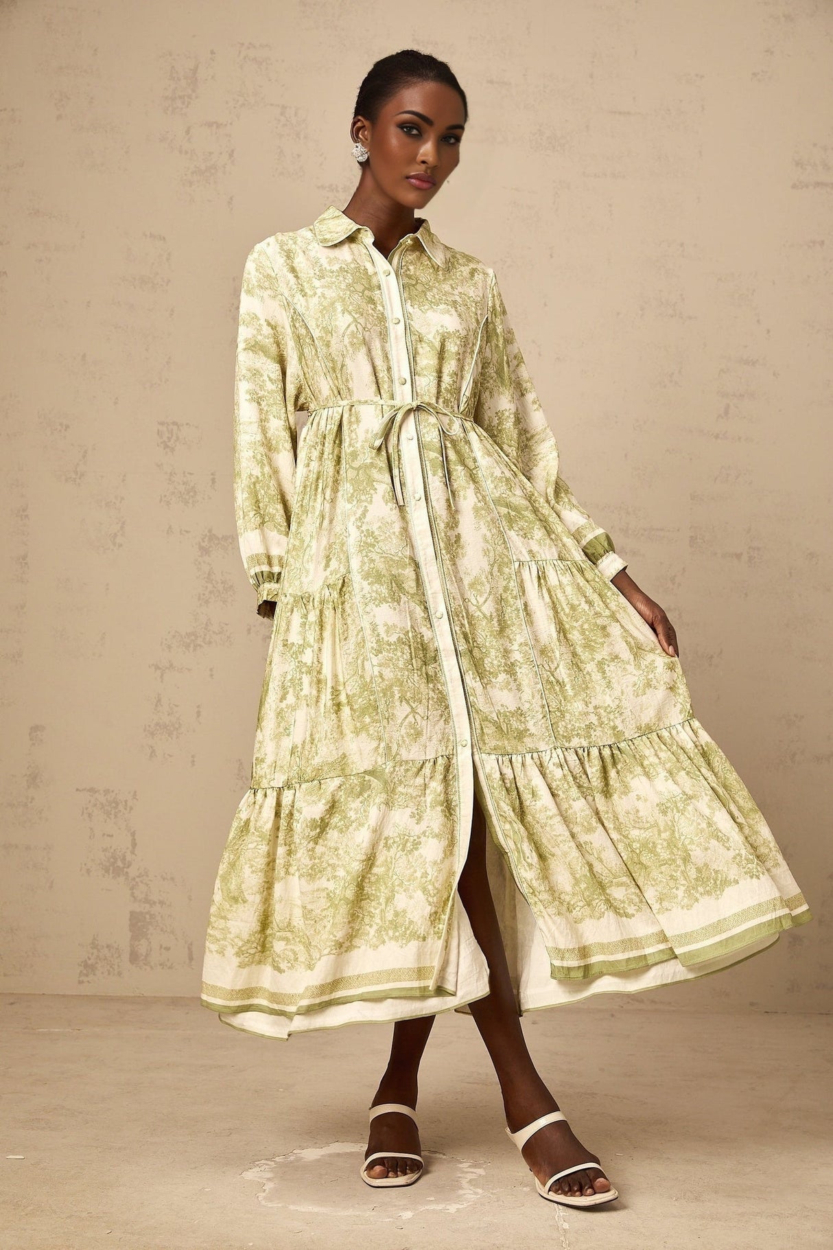 A green midi dress with a graphic print pattern featuring the Adélaïde design worn by a model standing in a neutral setting