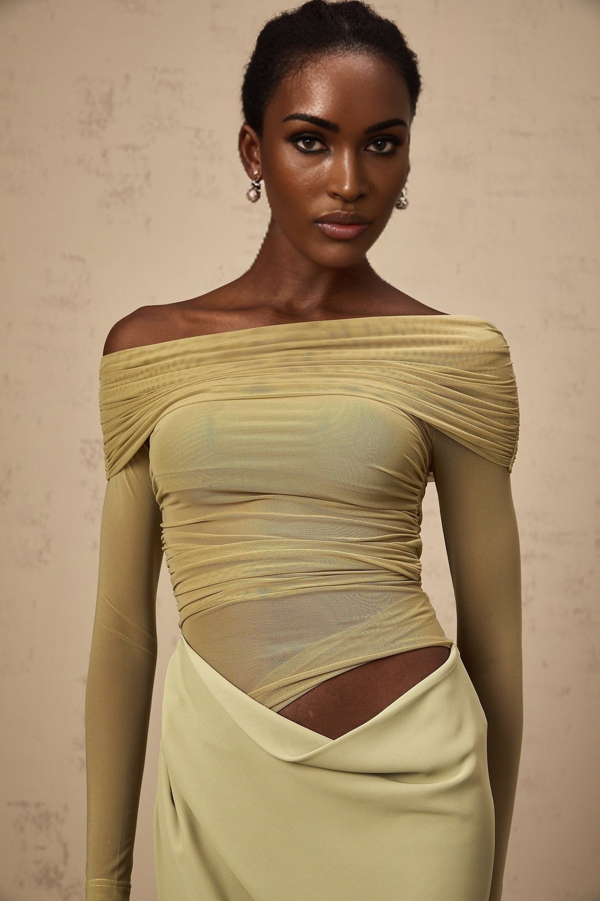 A green offshoulder midi dress with a semisheer fabric and a flowing silhouette worn by a model against a plain background
