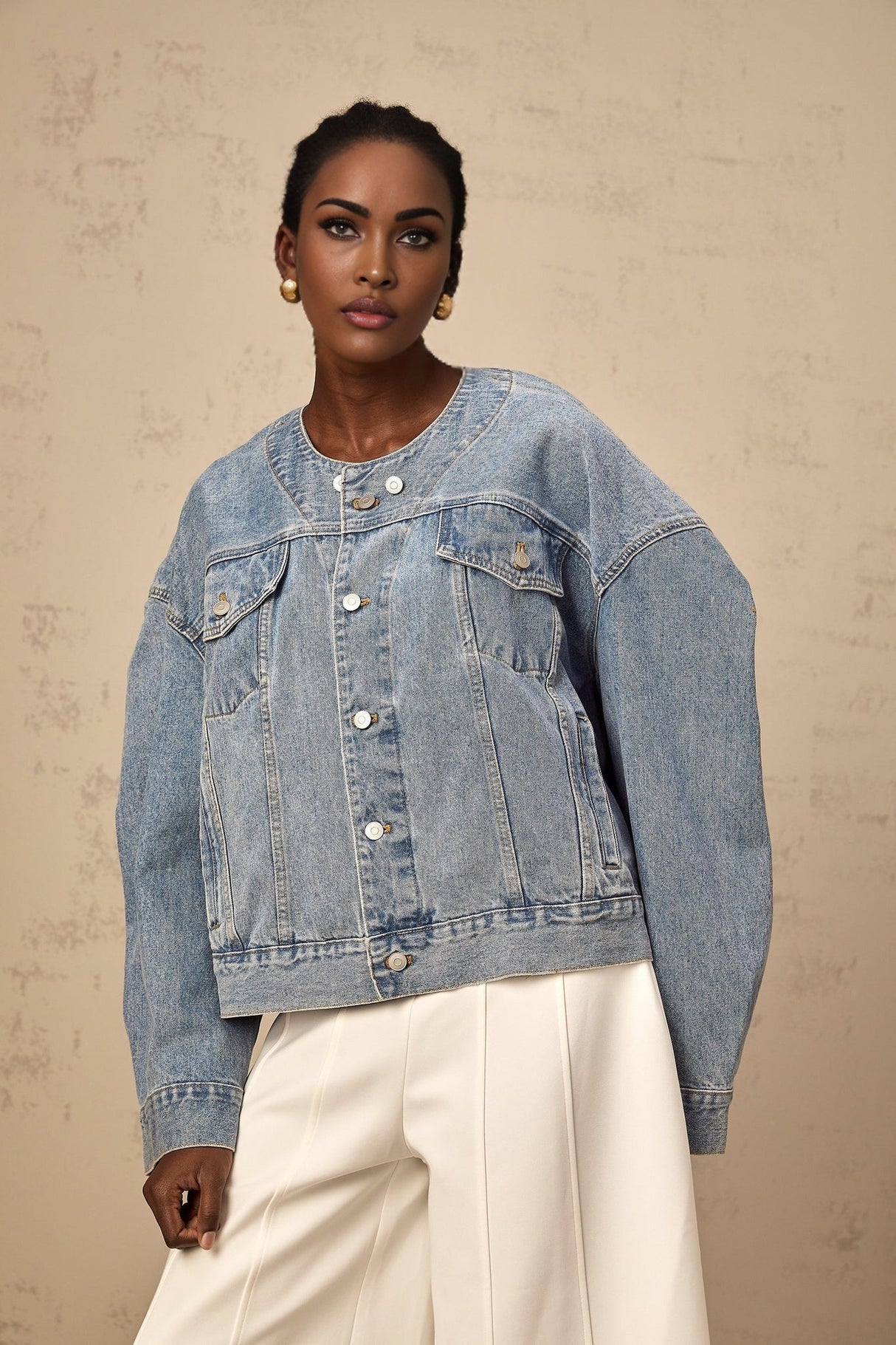 A light blue denim jacket without a collar worn by a woman against a plain background