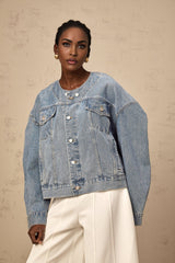 A light blue denim jacket without a collar worn by a woman against a plain background