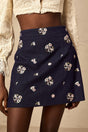 A light blue mini skirt with delicate flower embroidery featuring a short hemline and fitted waistband