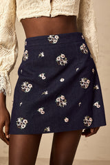 A light blue mini skirt with delicate flower embroidery featuring a short hemline and fitted waistband