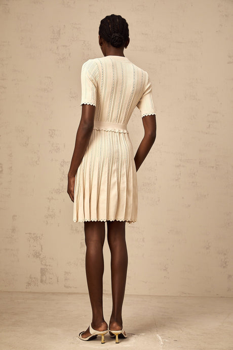 A lightcolored mini dress with a pleated knit design and delicate pointelle trim details along the edges