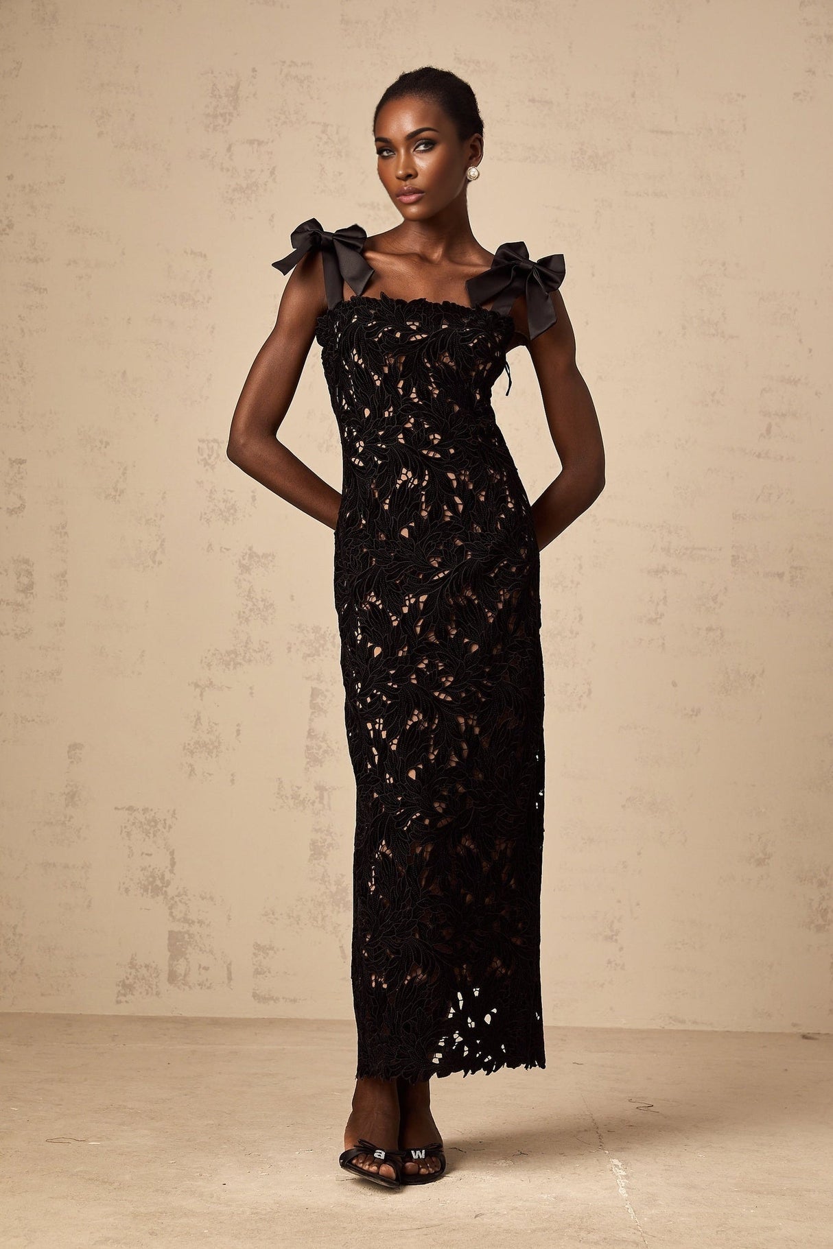 A long black maxi dress with colorful floral embroidery details worn by a model standing against a plain background