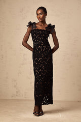 A long black maxi dress with colorful floral embroidery details worn by a model standing against a plain background
