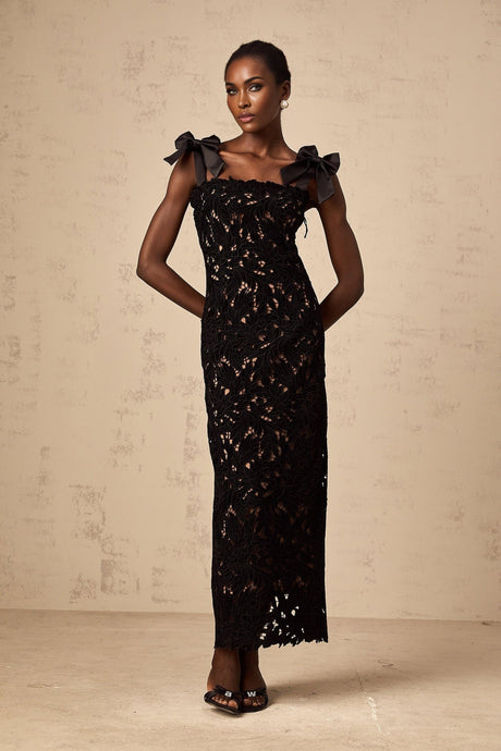 A long black maxi dress with colorful floral embroidery details worn by a model standing against a plain background