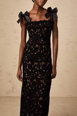 A long black maxi dress with colorful floral embroidery details worn by a model standing in a neutral background