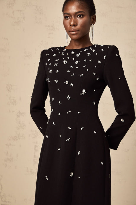 A long black maxi dress with crystal embellishments on the fabric sparkling against the dark background