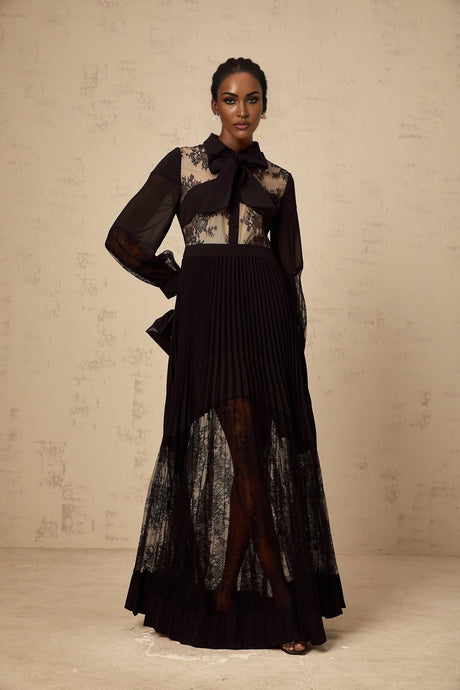 A long black maxi dress with pleated skirt and floral lace panels featuring a fitted bodice and flowing silhouette