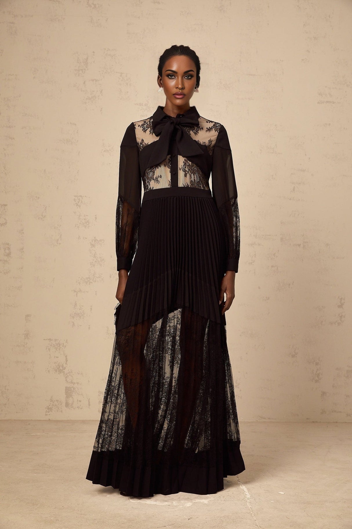 A long black maxi dress with pleats and floral lace panels featuring a feminine silhouette and elegant design