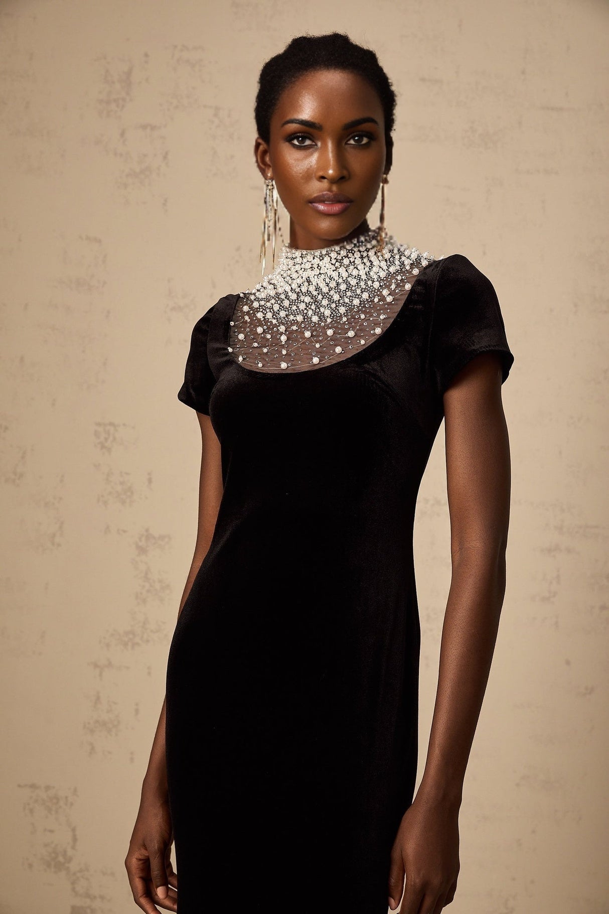A long black velvet maxi dress with faux pearl embellishments worn by a model against a plain background