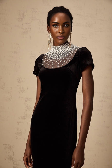 A long black velvet maxi dress with faux pearl embellishments worn by a model against a plain background