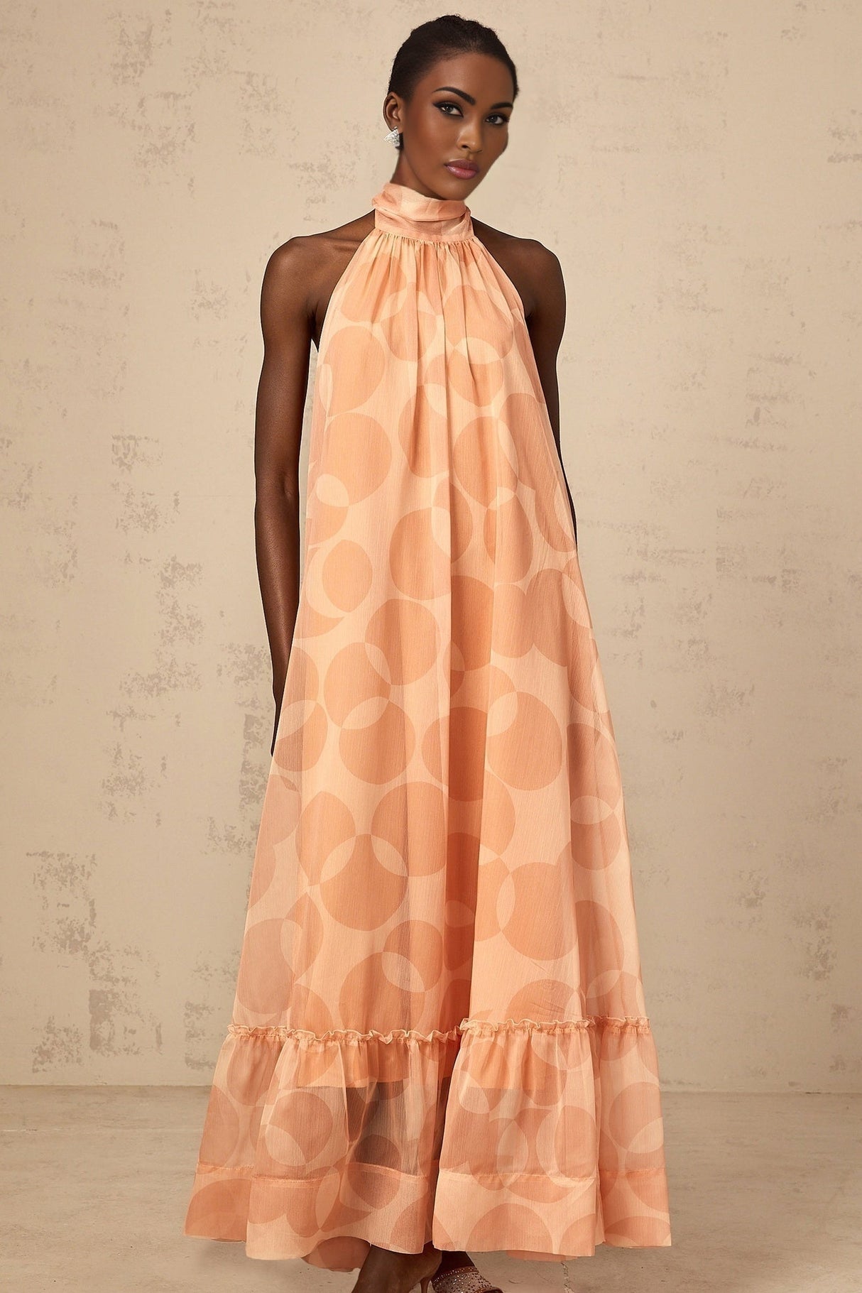 A long coralpink maxi dress with a halter neckline featuring an allover pattern print and a flowing silhouette