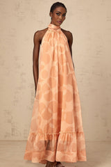 A long coralpink maxi dress with a halter neckline featuring an allover pattern print and a flowing silhouette