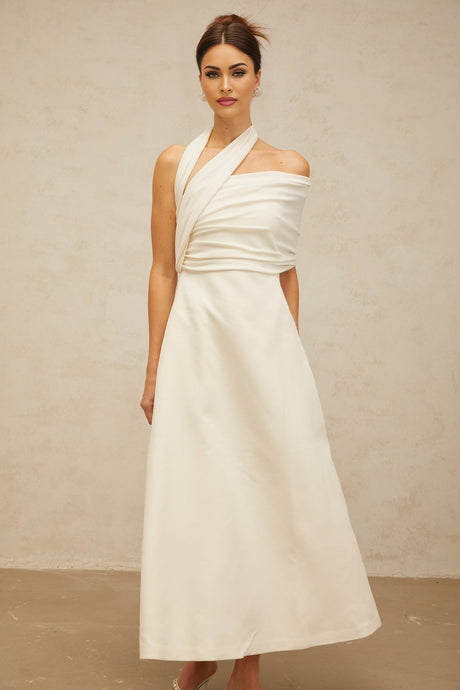 A long creamwhite maxi dress with an asymmetric design featuring a flowy skirt and uneven hemline worn by a model against a plain background