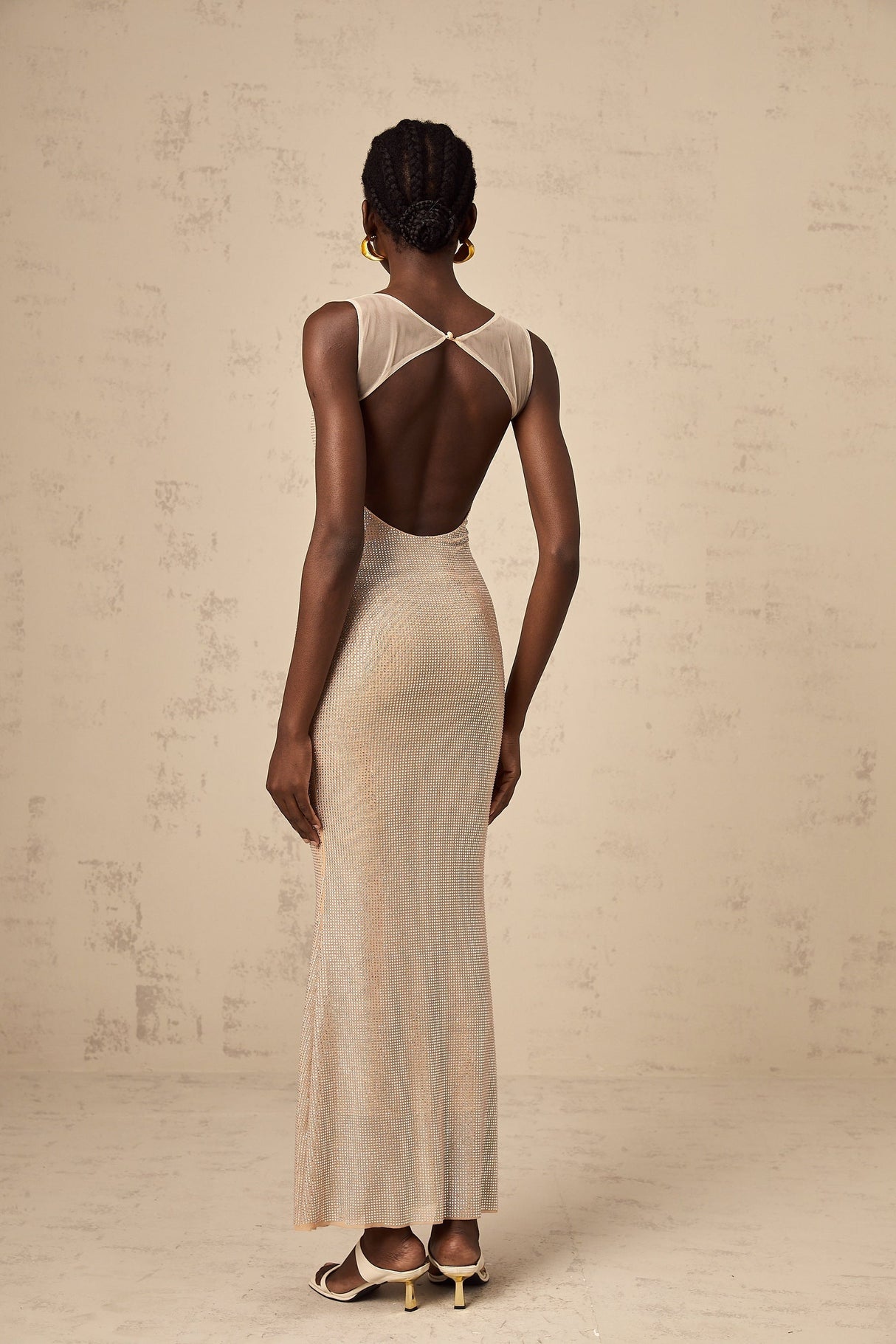 A long elegant maxi dress with crystal embellishments and an open back design featuring a flowy silhouette in a light color
