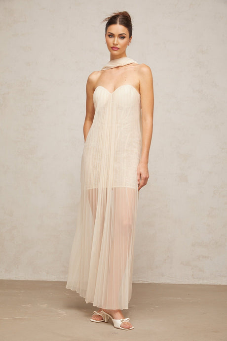 A long flowing maxi dress in neutral tones featuring a pleated tulle skirt and decorative ribbon design details