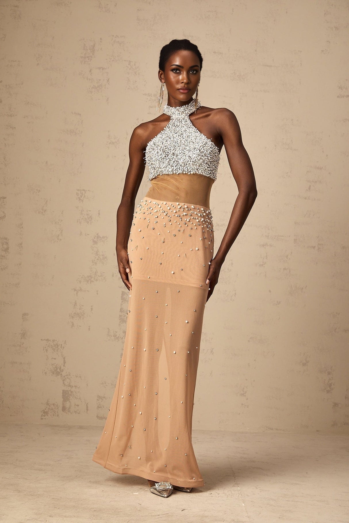 A long flowy maxi dress in a light color with sheer fabric and pearl decorations throughout