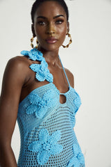 A long flowy maxi dress with intricate crochet detailing and decorative faux flowers throughout the design