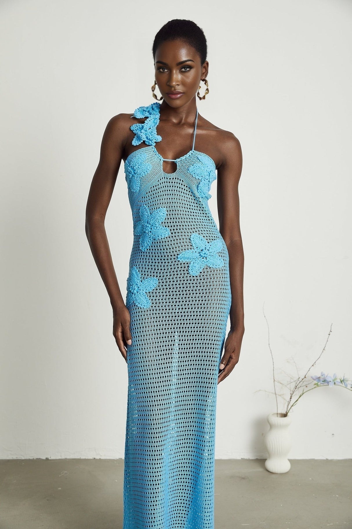 A long flowy maxi dress with intricate crochet details and colorful faux flowers adorning the bodice and skirt