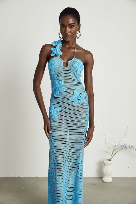 A long flowy maxi dress with intricate crochet details and colorful faux flowers adorning the bodice and skirt