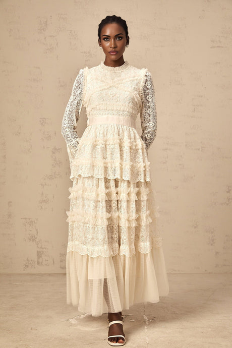 A long neutralcolored maxi dress with lace panels and ruffled tulle details featuring a flowing silhouette and delicate feminine design